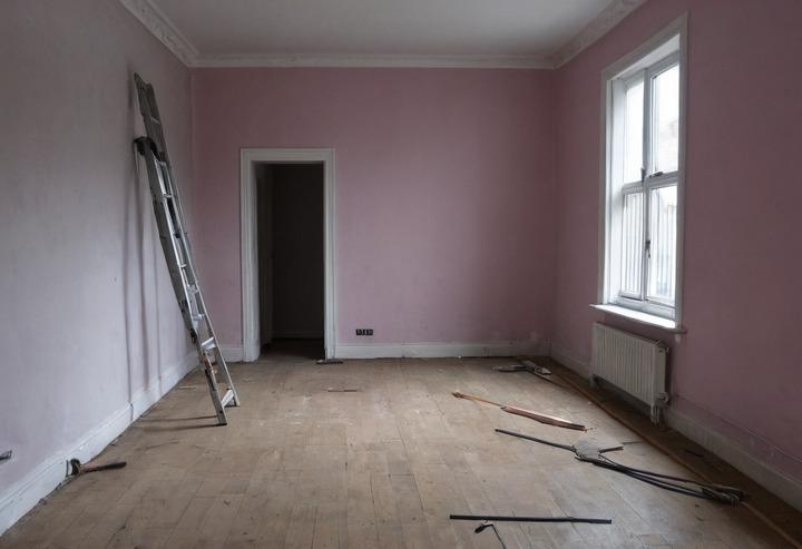 A partly renovated flat with new oak flooring laid across half the room, stacked flooring packs, a folded ladder and bare plastered walls.